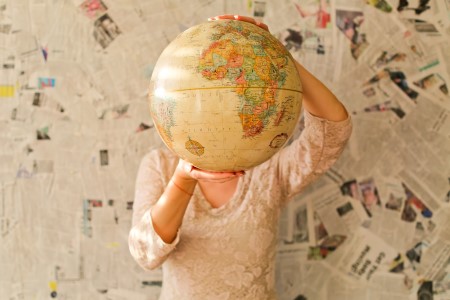 Person holding a globe, covering their face, on a background of newspaper clippings,