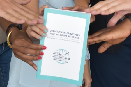 3 sets of hands, holding a turquoise "Democratic Principles for an Open Internet" pamphlet.